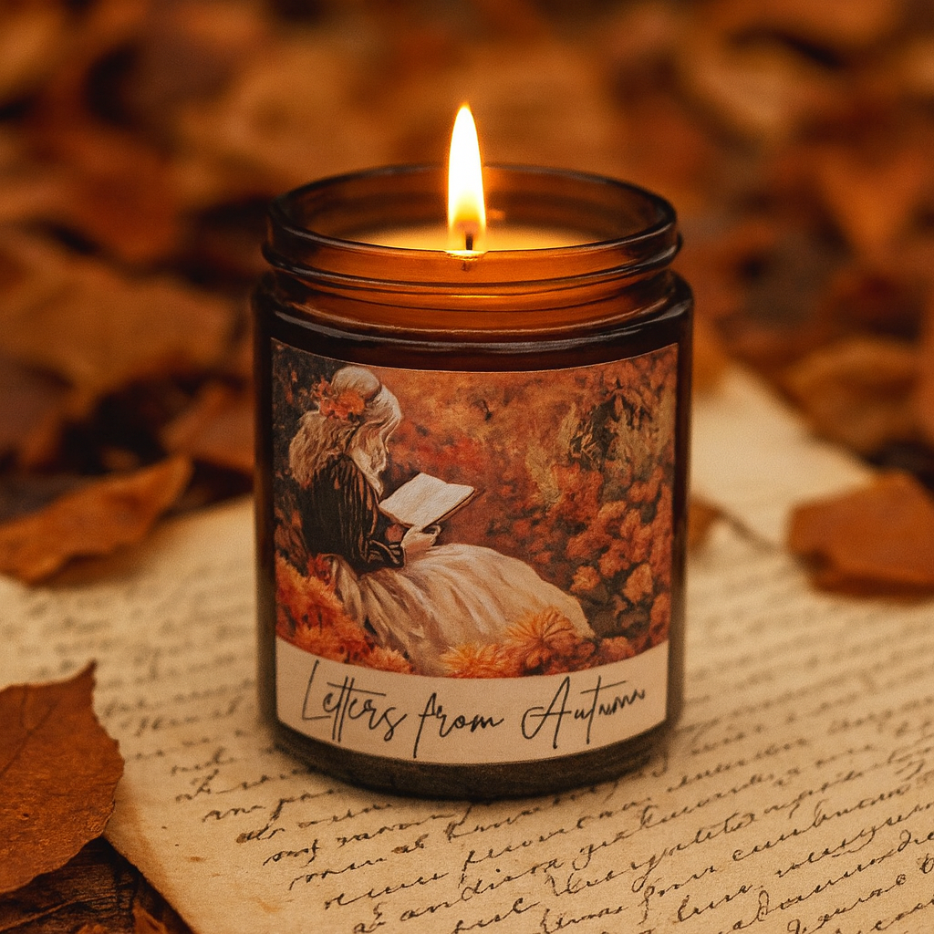 Candle in a jar labeled 'Letters from Autumn' on a surface with autumn leaves.