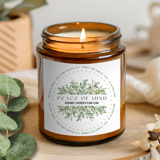 Candle in an amber jar with a 'Peace of Mind' label on a wooden surface with eucalyptus leaves.