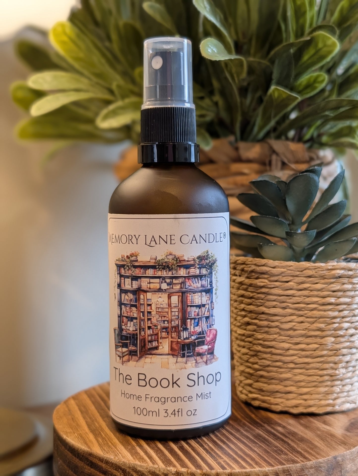 Bottle of 'The Book Shop' home fragrance mist by Memory Lane Candles on a wooden surface with plants in the background.
