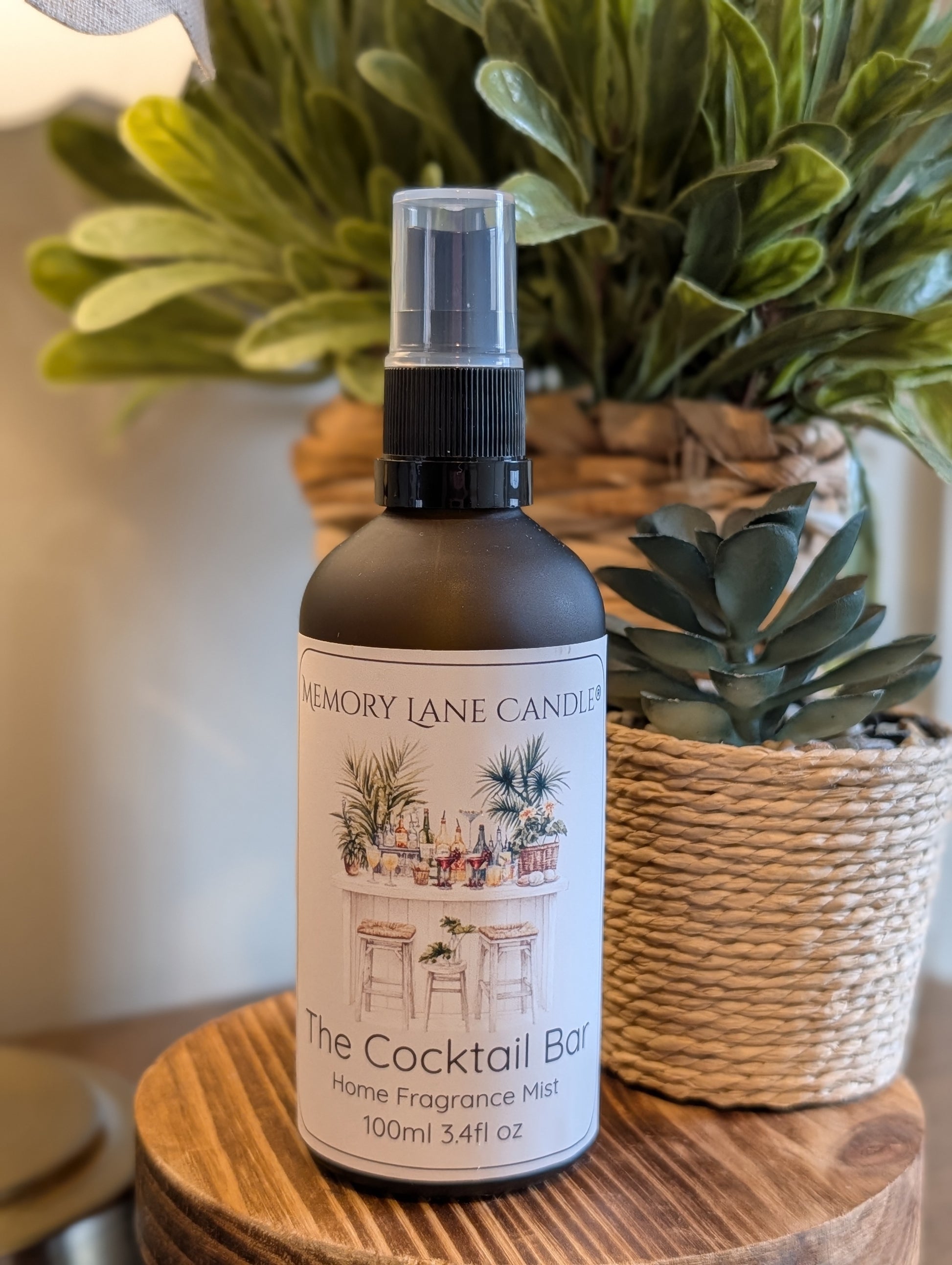 Home fragrance mist bottle labeled 'The Cocktail Bar' by Memory Lane Candles on a wooden surface with plants in the background.